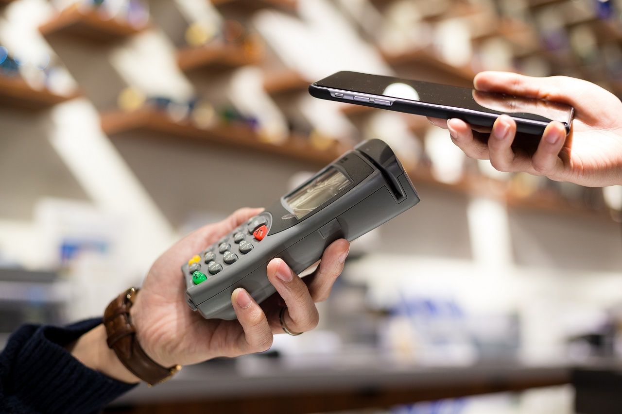 Uma mulher realizando uma venda usando uma maquininha de cartão de créditos por aproximação com um aparelho de celular.