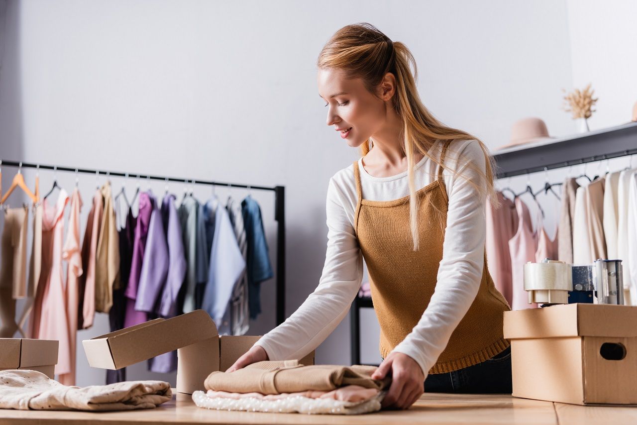 Mulher trabalhando em loja de roupa, empacotando mercadoria.