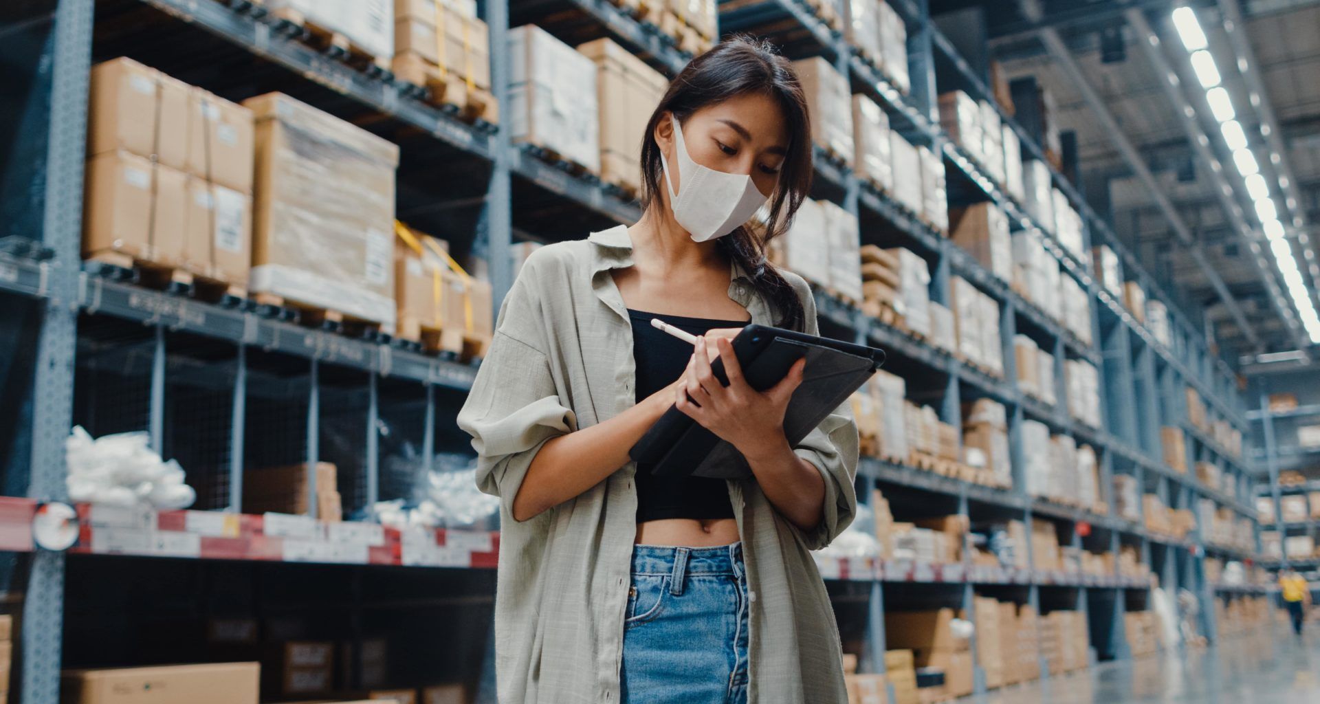Jovem mulher de negócios asiática usando máscaca checando o inventório do depósito.
