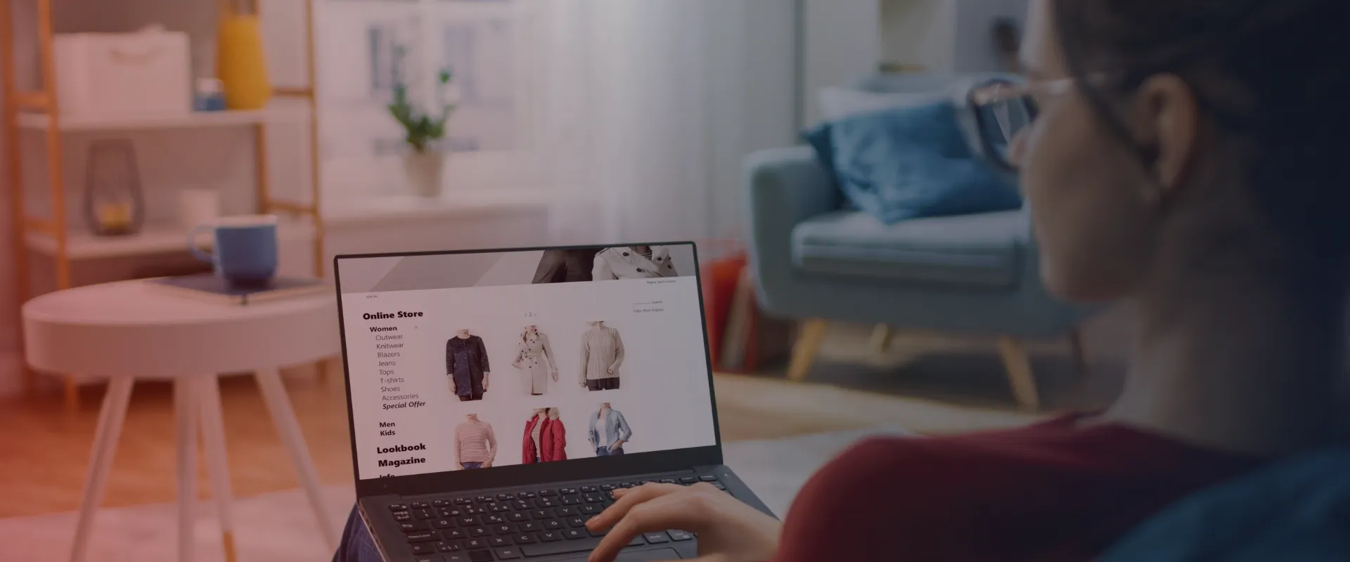 Esta imagem mostra uma pessoa comprando roupas femininas online em um laptop. Ela está usando a mão esquerda para navegar no site, que apresenta uma variedade de categorias, incluindo agasalhos, malh…