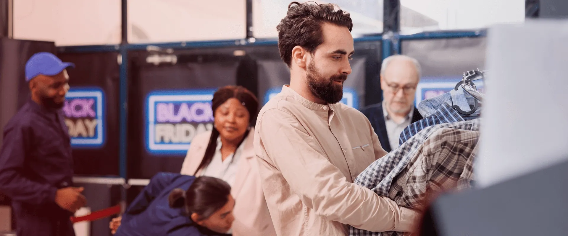 A imagem mostra um homem segurando vários casacos xadrez, olhando para eles enquanto se encontra em uma loja. Ele está na seção de roupas, e há um sinal azul brilhante que diz "Black Friday". Há outr…