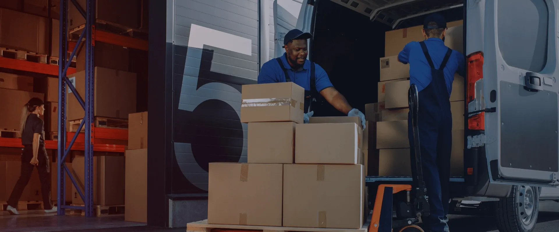 A imagem mostra dois homens carregando caixas marrons em uma van de entrega branca. Um homem está empilhando as caixas em uma plataforma e o outro está empurrando um carrinho de mão. Uma mulher está…
