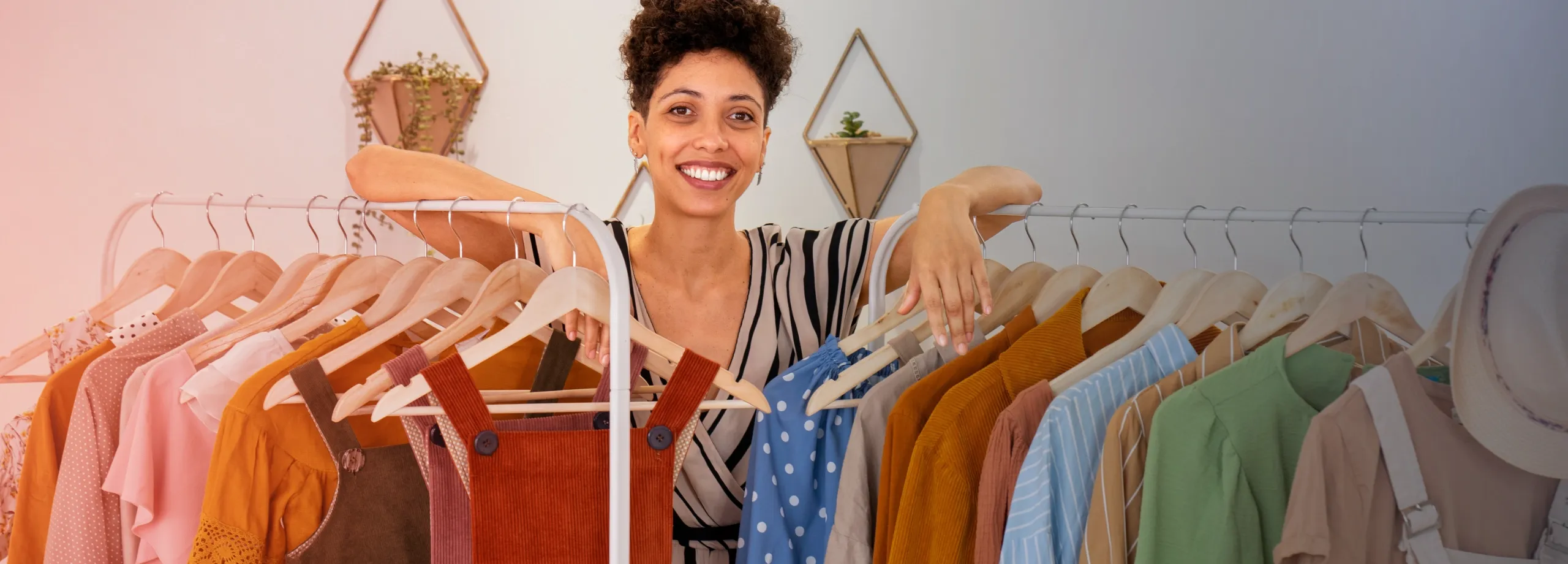 Uma mulher, rodeada de uma variedade de opções de roupa num varão, sorri para o espectador.