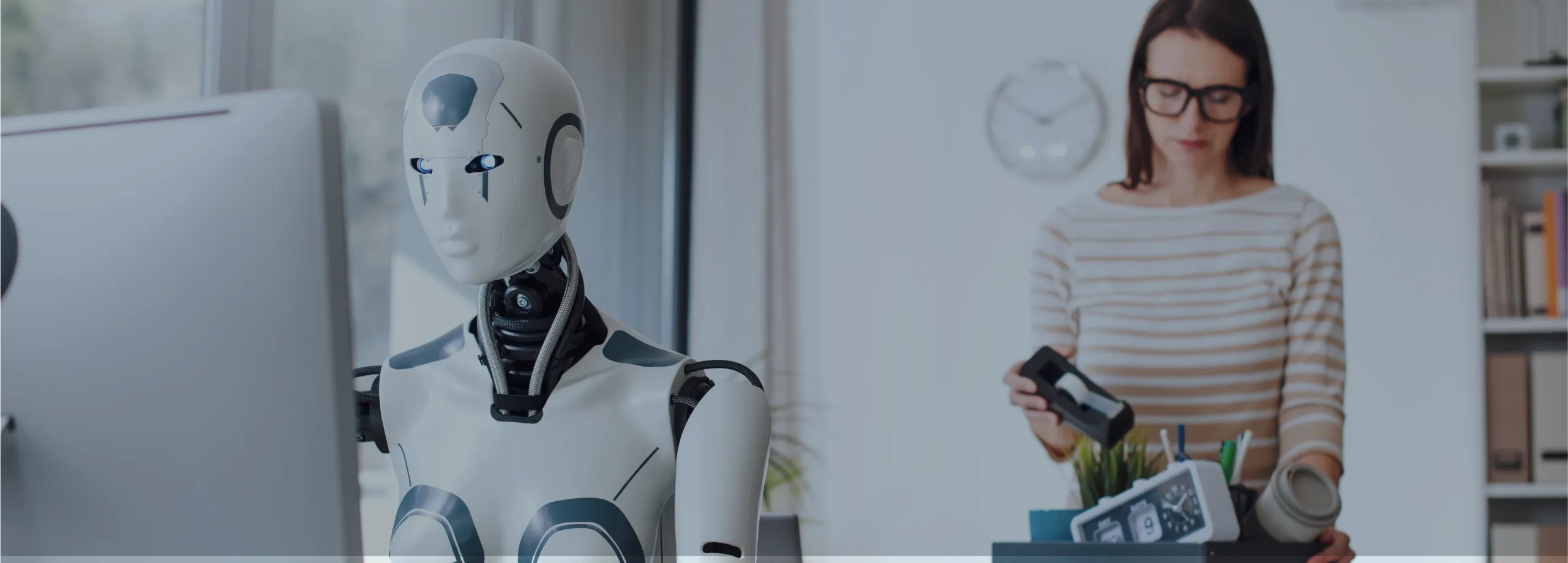 Cena em um escritório: à esquerda e em foco, um robô branco com traços humanos está sentado digitando em um computador. Ao fundo, levemente desfocada, uma mulher de óculos e blusa listrada está em pé…