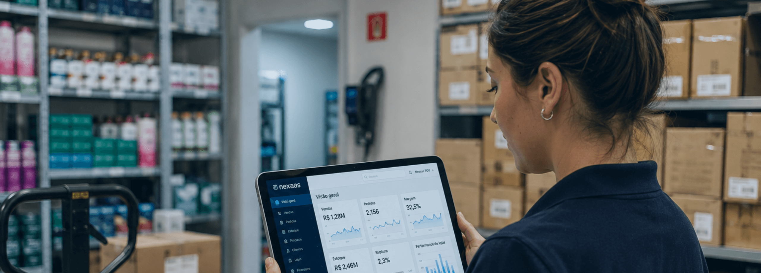 Uma mulher segura um tablet com gráficos e dados dentro de um estoque cheio de mercadorias.